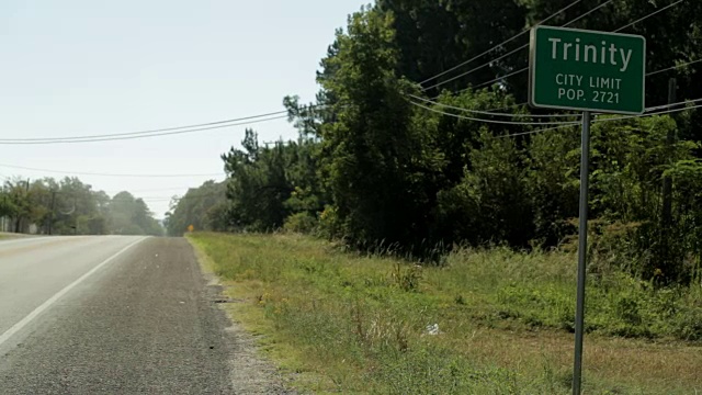 高速公路镇的标志，上面写着，“Trinity City Limit pop”。一辆车从公路上开过。视频素材