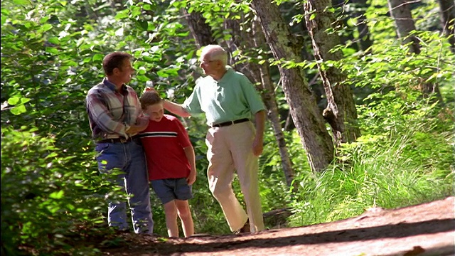 CANTED man, senior man + boy talking + walking in path in forest手臂挽手走在森林里的小路上视频素材