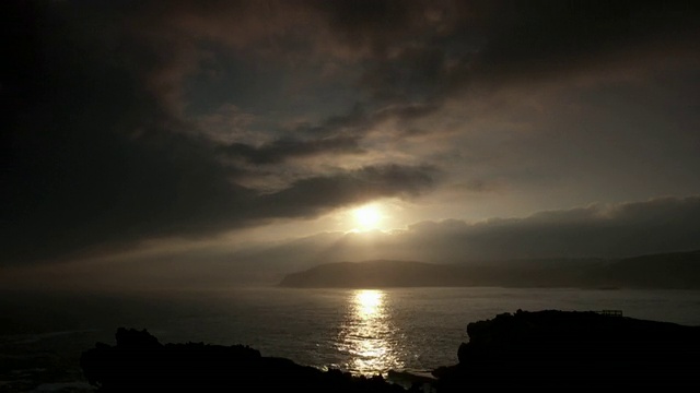 云朵在海岸山坡上的夕阳前掠过，然后变成了黑色。视频素材