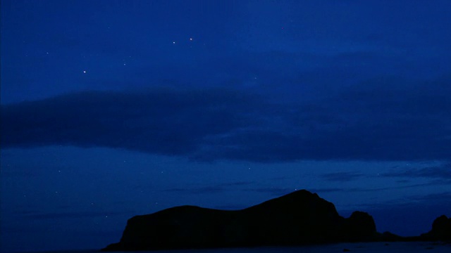 夜幕降临时，云层掠过岩石的轮廓，星星在海岸上盘旋。视频素材