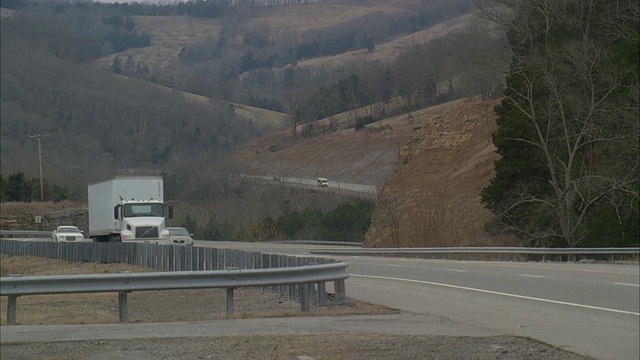 广角汽车、卡车和旅游巴士行驶在高速公路上穿越山区、农村地区。树上光秃秃的树枝。视频素材