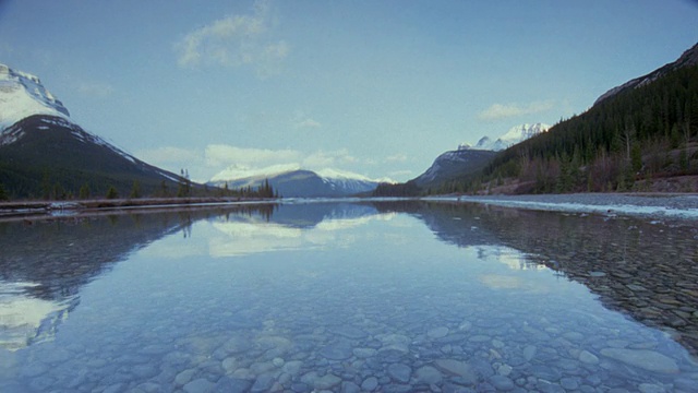 广角镜头的水与时间流逝云在积雪覆盖的落基山脉的背景/阿尔伯塔，加拿大视频素材