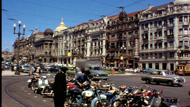 20世纪50年代的交通经过城市街道上的一排建筑，前景中有摩托车和摩托车视频素材