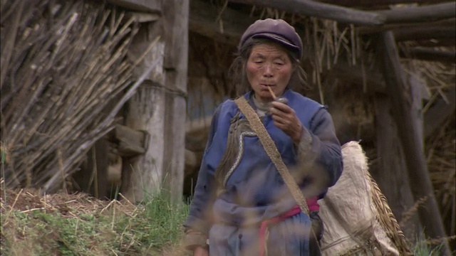 一名西藏妇女抽着烟斗，走过一幢废弃的农场建筑。视频素材