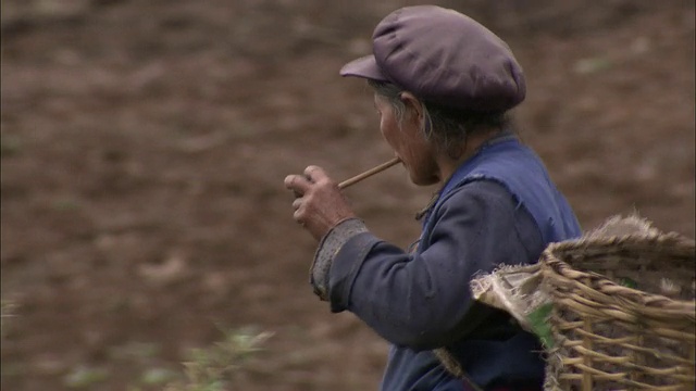 一位西藏妇女背着一个大篮子，一边走一边抽着烟斗。视频素材