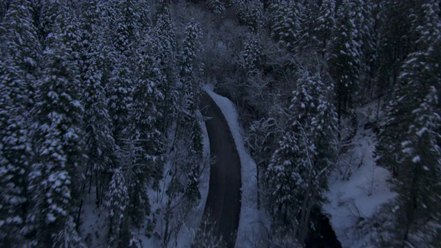 一条狭窄的道路蜿蜒穿过一条河流，穿过犹他州白雪覆盖、树木繁茂的瓦萨奇山脉。视频素材