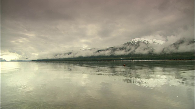 在阿拉斯加，平静的水面反映出白雪皑皑的海岸线和低矮的云层。视频素材