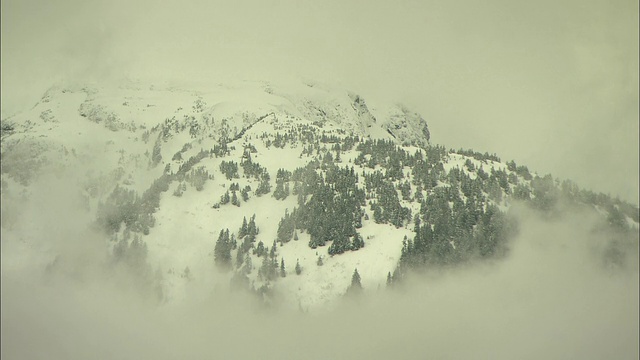 低空的云朵环绕着树木繁茂的湖泊和雪山。视频素材