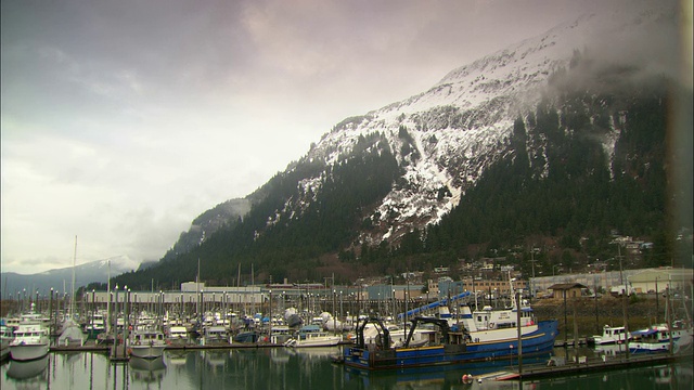 船只停靠在阿拉斯加多雪的多山海岸的一个码头上。视频素材