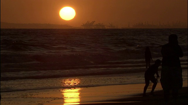 海滩上的夕阳映出游客们在潮湿的沙滩上漫步的剪影。视频素材