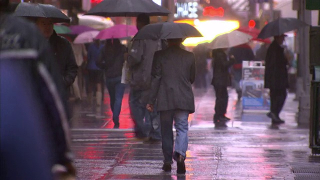 雨中，行人撑着雨伞走在繁忙的人行道上。视频素材