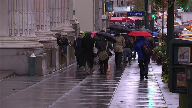 撑着雨伞的行人走近纽约市人行道上的东34街指示牌。视频素材