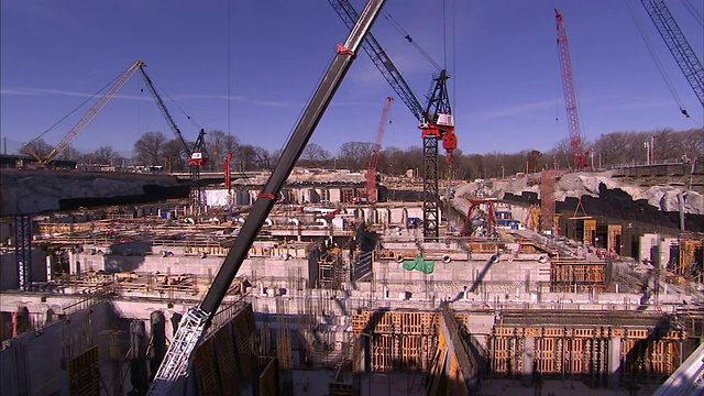 建筑起重机在一个大型建筑工地的高空作业，建筑工人从栏杆上看过去。视频素材