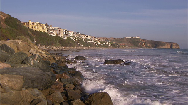 海浪滚向房屋附近的岩石海岸。视频素材