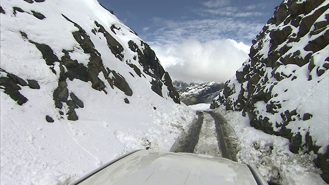 一辆卡车缓慢地行驶在秘鲁山区一条被积雪覆盖的狭窄道路上。视频素材