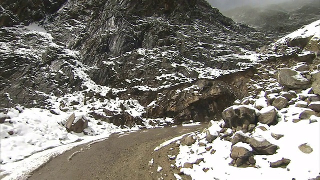 在秘鲁，一条狭窄的土路蜿蜒穿过多岩石的雪山。视频素材