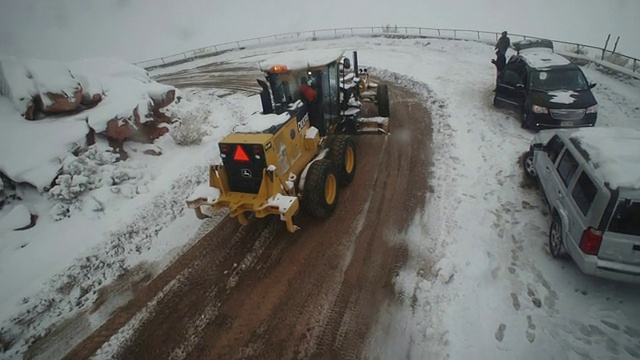 一辆扫雪机在泥泞的道路上缓缓移动，经过停在雪地里的两辆汽车。视频素材