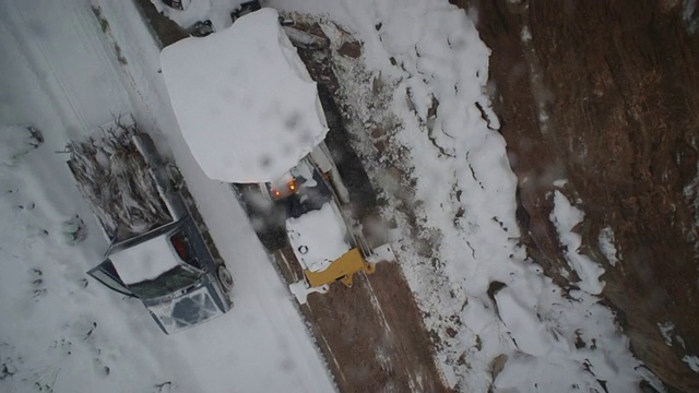 一辆刨雪机和一辆半卡车在山区一条多雪的狭窄道路上行驶。视频素材