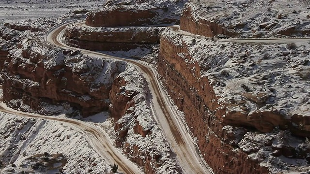 一辆卡车在积雪覆盖的悬崖上的狭窄道路上行驶。视频素材