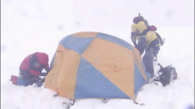 在暴风雪中，穿着冬装的徒步旅行者稳住帐篷的角落。视频素材