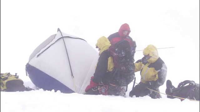 穿着冬装的徒步旅行者在暴风雪中搭起了帐篷。视频素材