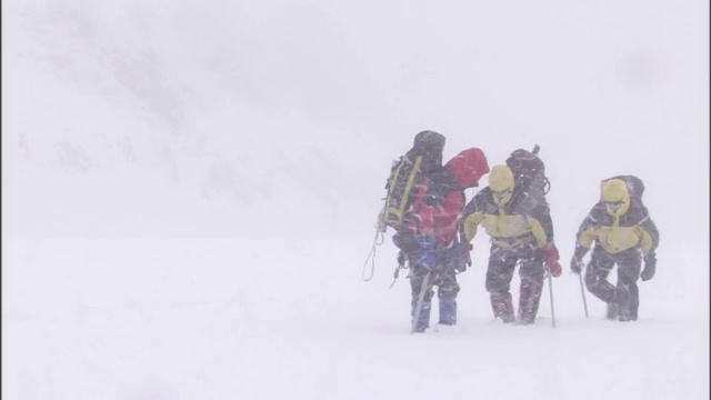 在暴风雪中，穿着冬装背着大背包的徒步旅行者在厚厚的积雪中跋涉。视频素材