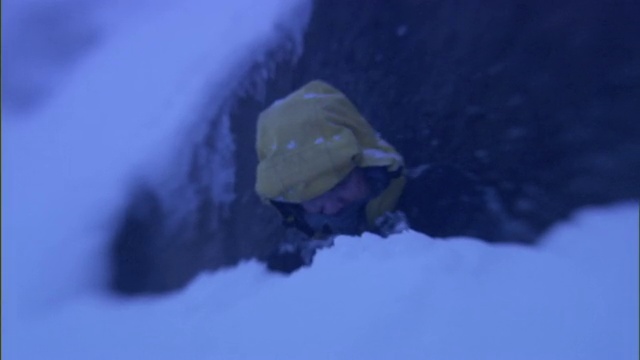 一个戴着兜帽、围巾和手套的男人在暴风雪中瑟瑟发抖。视频素材