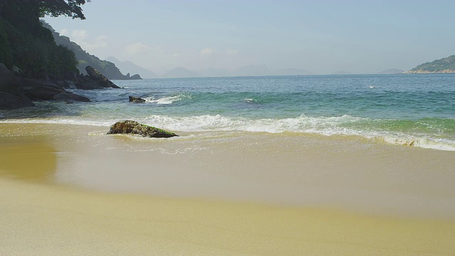 在里约热内卢的红海滩，海浪在沙滩上的一块巨石周围退去和流动的缓慢运动。视频素材