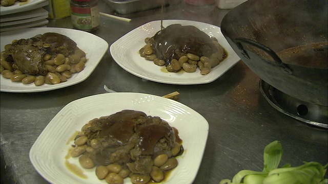 在餐馆的厨房里，厨师们用勺子把食物盛到盘子里。视频素材