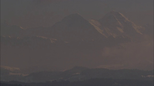 浓雾在白雪覆盖的山脚下的森林中飘过。视频素材