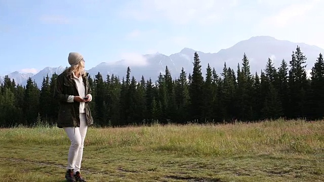 女人沿着小径穿过草地，身后是连绵的山脉视频素材