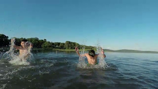 快乐的孩子们在湖边戏水，与闪闪发光的夕阳形成对比。视频下载