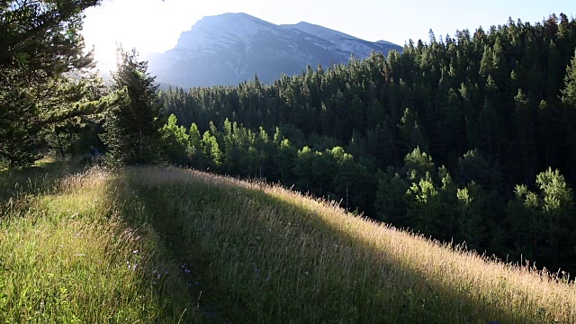 山地自行车穿过草地，太阳从后面的山上升起视频素材