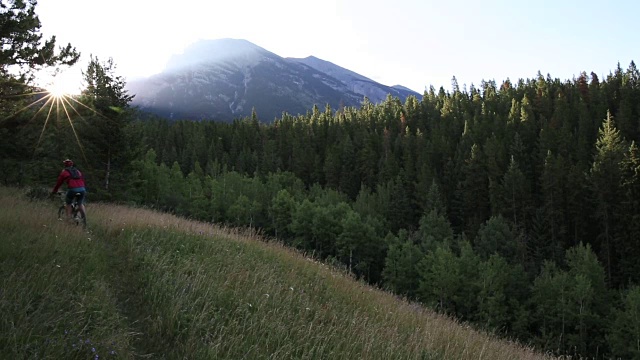 山地自行车穿过草地，太阳从后面的山上升起视频素材