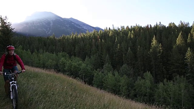 山地自行车穿过草地，太阳从后面的山上升起视频素材