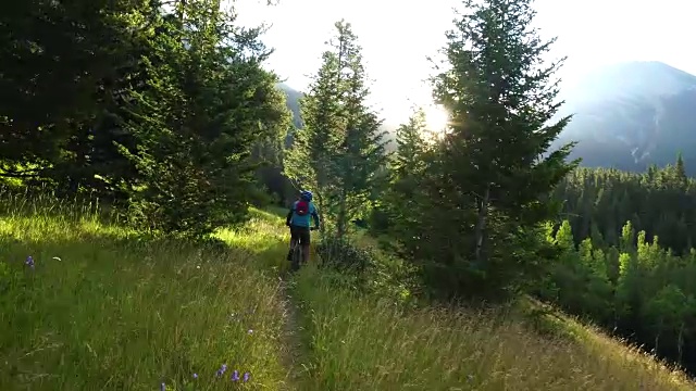 山地自行车穿过草地，太阳从后面的山上升起视频素材