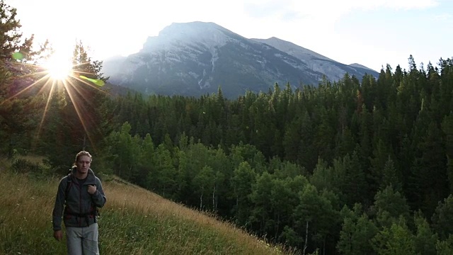 徒步旅行者沿着小径穿过草地，眺望高山和森林视频素材