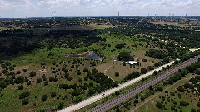 后面的汽车在德克萨斯州乡村的土路上行驶，远处有风电场视频素材