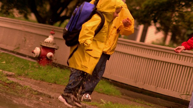 小男孩在水坑里跑+跳，大男孩和女孩在一旁看着视频素材