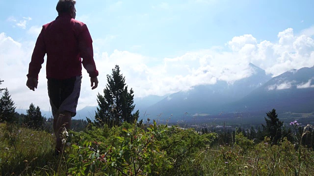 男性徒步旅行者穿过长满草的山脊，眺望群山视频素材