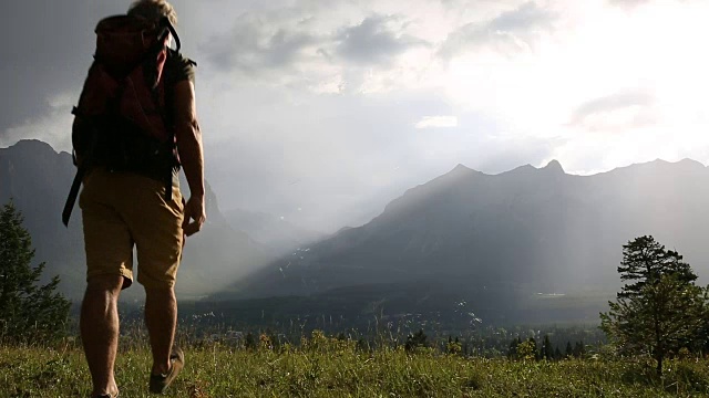 一名男性徒步旅行者穿过高山草地，停下来欣赏风景视频素材