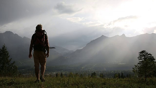 一名男性徒步旅行者穿过高山草地，停下来欣赏风景视频素材