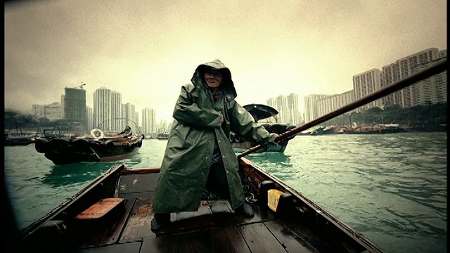 高反差的人在兜帽雨衣掌舵船+手势/船+建筑背景/香港视频素材