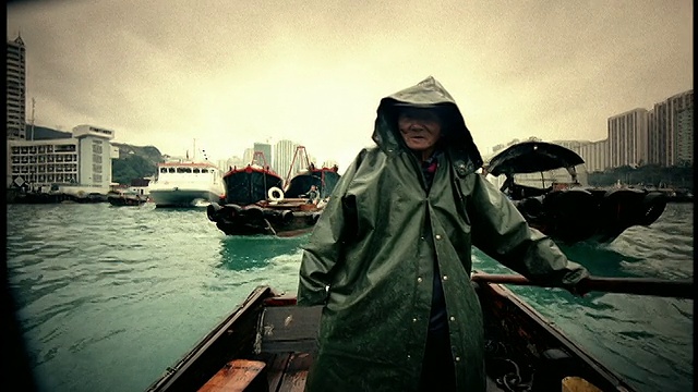 高对比度的MS男人穿着连帽雨衣掌舵船，说话+手势/船在背景/香港视频素材