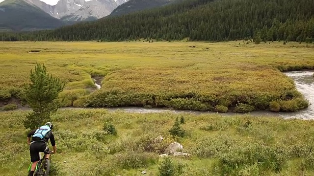 骑山地车的人沿着草甸斜坡，沿着小溪视频素材