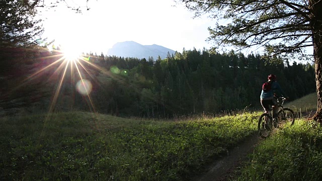 骑山地自行车的人沿着小路穿过草地，望向群山和森林视频素材