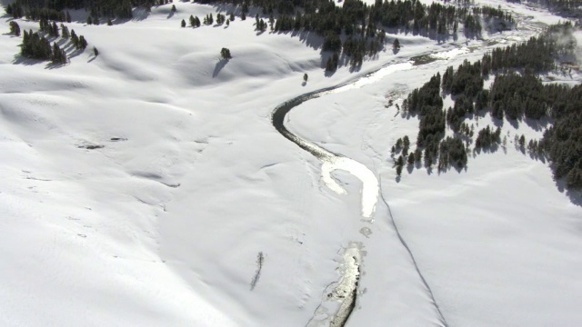 美国黄石国家公园山谷里积雪覆盖的河流上空的空中轨道视频素材