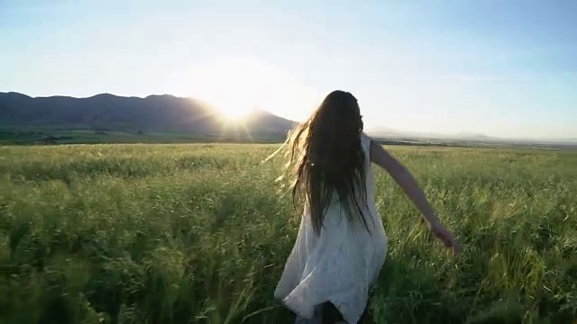 长发女孩在夕阳下穿过麦田。视频素材