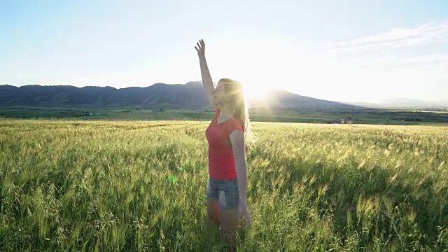 日落时分，一名年轻女子在草地上举起双手视频素材