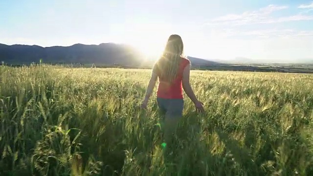 一个年轻的女人在夕阳下穿过田野视频素材